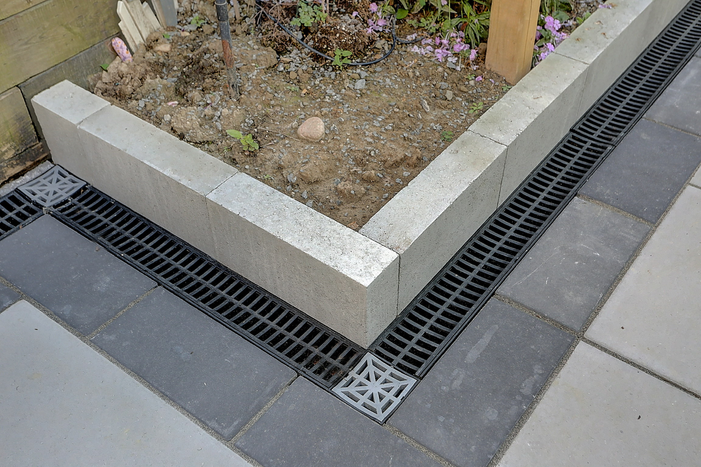 Channel drainage system installed beside interlocking pavers and a garden bed