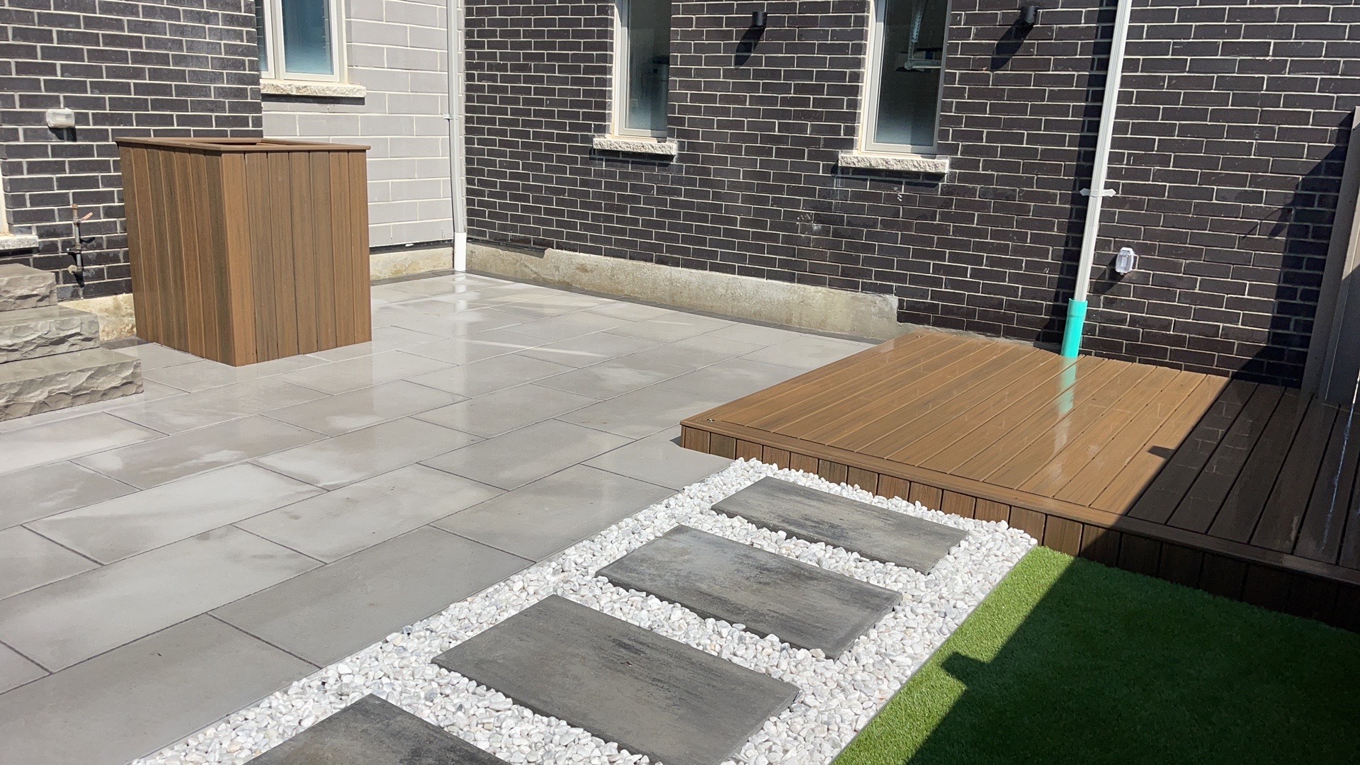 Low-maintenance backyard with interlocking patio, artificial grass, composite deck, and decorative stone